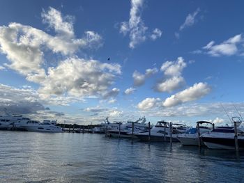 Boats moored at harbor against cloudy sky