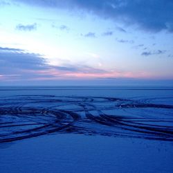 Tire tracks on frozen lake against sky during sunset