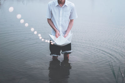 Young man holding paper boat with lights in lake