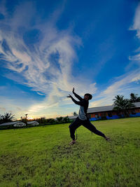 Rear view of man skateboarding on field against sky