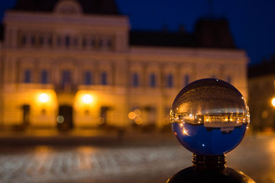 Close-up of metal sphere with reflection of illuminated building at night