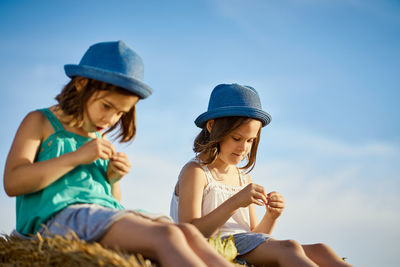 Low angle view of friends wearing hats sitting against sky