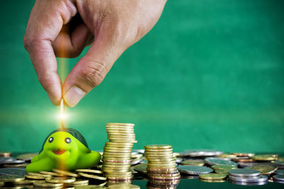 Cropped hand of person putting coin in piggy bank on table