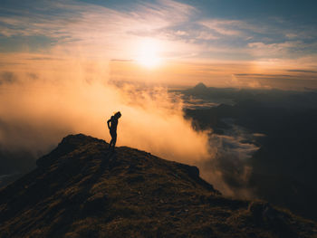 Woman standing on rock at mountain against sky during sunrise