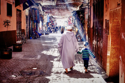 Rear view of grandfather and boy walking on street in town