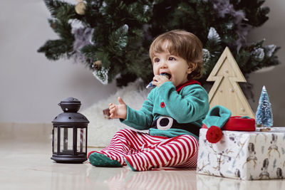 A little 12-month-old christmas elf with a christmas tree and gifts