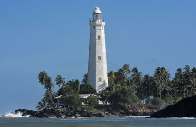 Low angle view of lighthouse by sea against clear blue sky