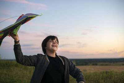 Portrait of young woman with arms raised standing against sky during sunset