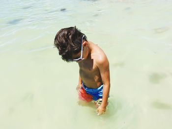 Shirtless boy wearing sunglasses in sea on sunny day