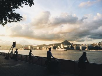 People by sea against sky during sunset