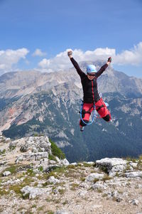 Rear view of man jumping on mountain against sky