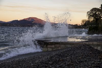 Waves splashing on rocks against sky during sunset