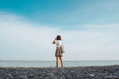 Rear view of woman standing on beach against sky