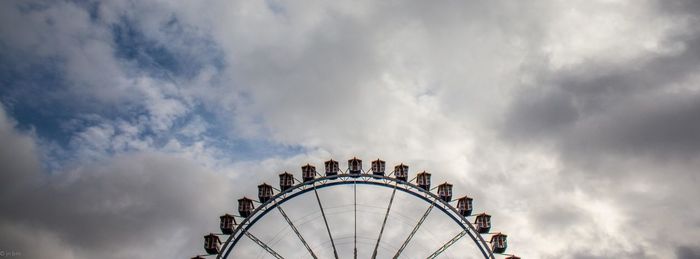Low angle view of ferris wheel against cloudy sky