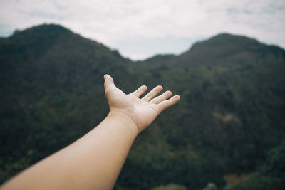 Cropped hand gesturing against mountain