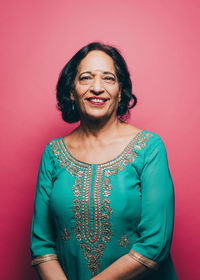 Portrait of smiling senior woman wearing salwar kameez against pink background