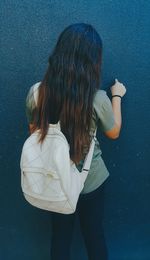 Rear view of woman with bag standing against wall