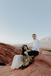 Young woman sitting on rock against clear sky