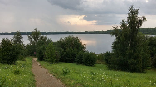 Footpath by river against cloudy sky