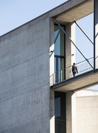 Low angle view of man standing on elevated walkway amidst building