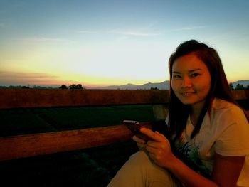 Young woman using smart phone against sky during sunset
