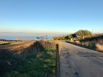 Empty road amidst field against clear sky