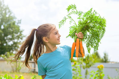 Smiling little girl in a green t-shirt holds a bunch of fresh carrots,