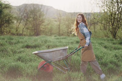 Portrait of cheerful woman with wheel barrow at farm