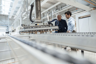 Young businessman discussing with colleague over machinery at factory