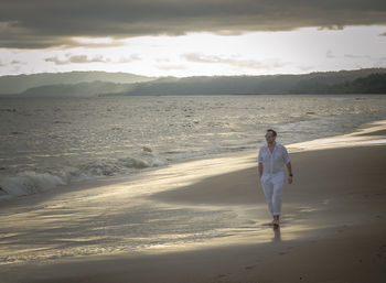 Rear view of woman walking on beach against sky during sunset