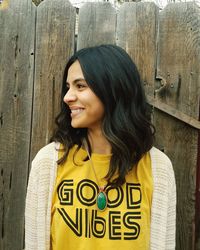 Portrait of smiling young woman standing against wooden wall