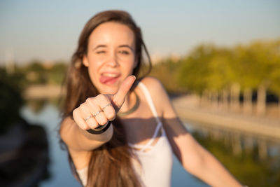 Portrait of young woman showing thumbs up sign by lake