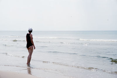 Side view of woman wearing swimwear standing at beach against clear sky