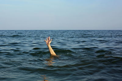 Cropped hand of man coming through sea water against sky