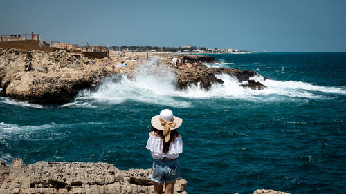 Woman standing on rock by sea against clear sky