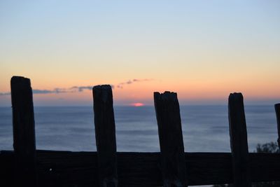 Silhouette wooden posts on beach against sky during sunset