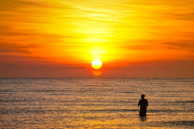 Silhouette man standing on sea against orange sky