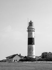 Lighthouse on field by building against sky