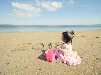 Side view of girl sitting on shore at beach against sky