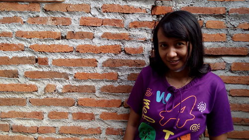 Portrait of smiling woman against brick wall