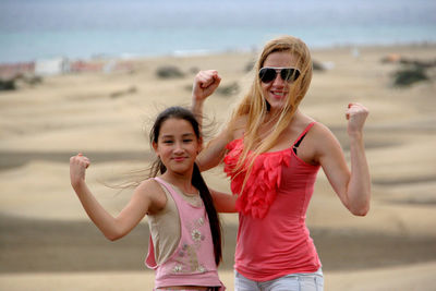 Portrait of smiling woman with daughter flexing muscles at beach 