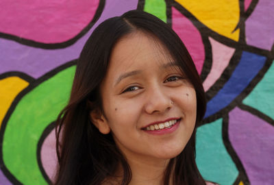 Portrait of smiling young woman against graffiti wall