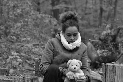 Sad woman holding stuffed toy while sitting in forest