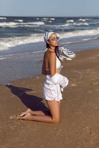 Woman in a white swimsuit and hat sunglasses on an empty sandy beach