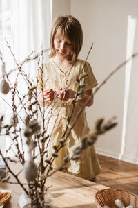 A girl decorates a bouquet of willow with easter eggs at home. decorating your home for the holidays