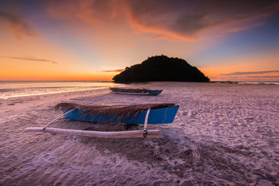 Boats at sandy beach against sky during sunset