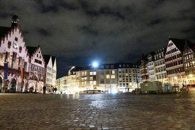 Illuminated buildings by street against sky at night