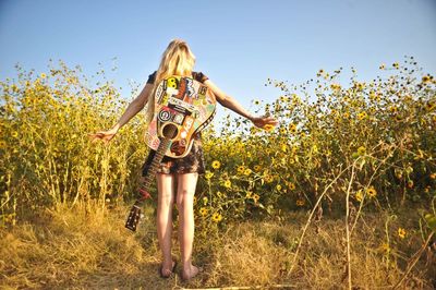 Woman with guitar standing on field against sky