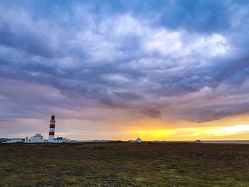 Lighthouse on beach against sky during sunset