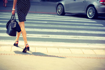 Low section of fashionable woman carrying bag while walking on street in city